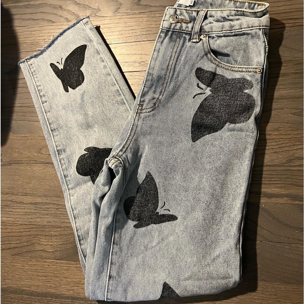 Medium wash straight leg jeans with butterfly details and distressed bottom.